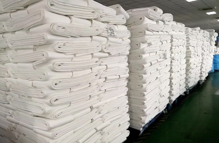 Hundreds of baghouse filter bags stacked on pallets in a row.